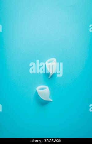 Coppia di tazze mestruali bianche su una superficie blu brillante. Composizione semplice e pulita che simboleggia l'igiene femminile sostenibile e lo stile di vita moderno choi Foto Stock