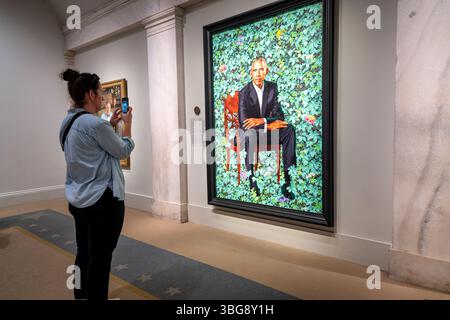 Barack Obama Ritratto di Kehinde Wiley nella National Portrait Gallery di Washington DC | WASHINGTON D.C., Stati Uniti — Un visitatore fotografa il ritratto ufficiale di Kehinde Wiley di Barack Obama alla National Portrait Gallery, dove il 44° presidente siede tra fitte fogliame verde e fiori. Completato nel 2018, il dipinto si allontanò nettamente dalla ritrattistica presidenziale tradizionale e divenne una delle opere più visitate della galleria. Si trova all'interno della collezione ospitata nell'Old Patent Office Building, l'unico set completo di ritratti presidenziali fuori dalla Casa Bianca. Foto Stock