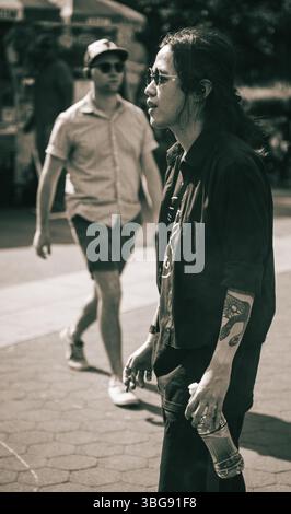 Uomo tatuato in occhiali da sole con bottiglia di bevanda in una strada della città - Candid Urban Editorial Portrait Foto Stock