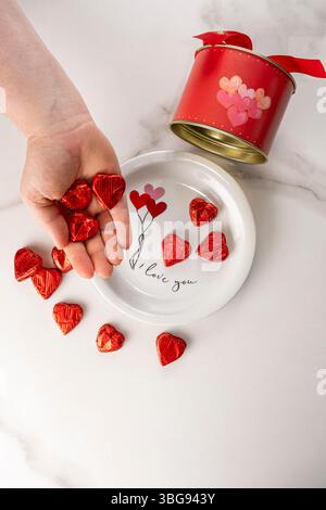 Donna che tiene cioccolatini a forma di cuore accanto a una scatola circolare rossa verticale. Foto Stock