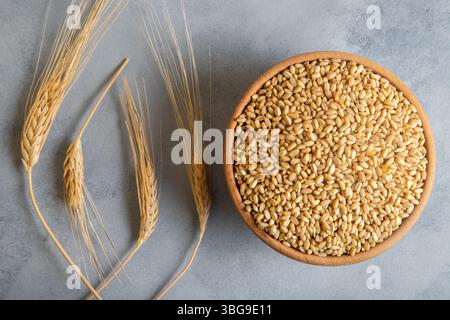 Grani di grano in una ciotola di legno e orecchie su sfondo luminoso, vista dall'alto Foto Stock