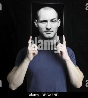 Il giovane tiene una foto di se stesso davanti al suo volto Foto Stock