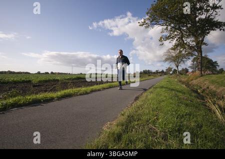Uomo di mezza età che fa jogging su un sentiero asfaltato in un'area rurale in prospettiva a basso grandangolo, Blomberg, Germania, Europa Foto Stock