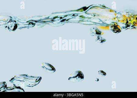 Vista laterale di una superficie d'acqua increspata mescolata con olio vegetale e bolle lievitanti isolate su uno sfondo azzurro Foto Stock