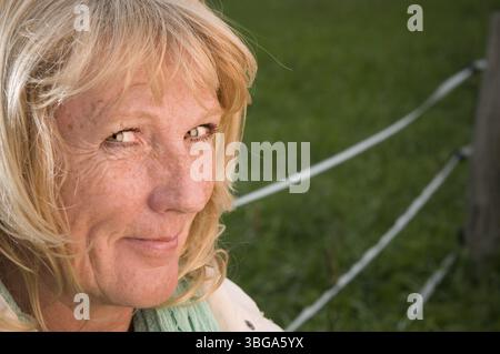 Primo piano laterale di una bella e bionda donna di mezza età davanti a un prato verde che appare incosciente nella fotocamera Foto Stock