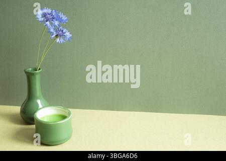 Tè verde e vaso di fiori viola sul tavolo. sfondo parete verde Foto Stock