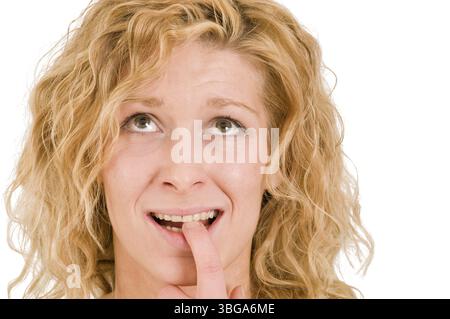 Ritratto frontale di una giovane donna bionda dai capelli ricci su sfondo bianco che tiene l'unghia sinistra tra i denti e lo sguardo Foto Stock