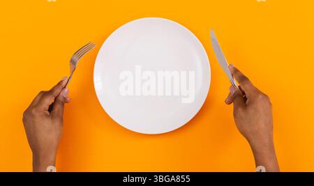 Femmina nero mani tenendo la piastra a vuoto su sfondo arancione, vista dall'alto, spazio libero Foto Stock