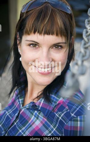 Ritratto laterale della testa e delle spalle di una giovane donna bruna con capelli dritti e occhiali da sole spinti sulla testa, sorridendo apertamente nella fotocamera. Ele Foto Stock
