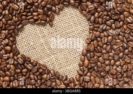 Vista che riempie il formato di una cornice inclinata a forma di cuore composta da chicchi di caffè tostati su un panno Foto Stock