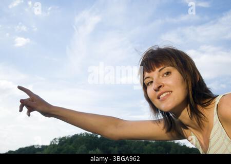 Foto della parte superiore del corpo di una giovane donna dai capelli castani di media lunghezza in una cima senza maniche in piedi in un lago di Potsdam (Griebnitzsee) e che punta con il suo ri Foto Stock
