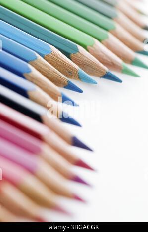 Primo piano di matite colorate disposte a onde su sfondo bianco con messa a fuoco sulle matite blu nella parte superiore dell'immagine Foto Stock