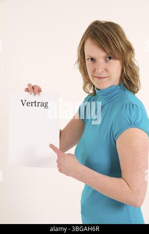 La donna bionda mostra con il dito indice al contratto in bianco, la giovane donna bionda punta con il dito indice a un contratto vuoto, Berlino, Germania, E. Foto Stock