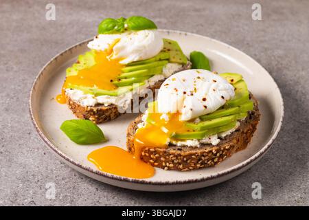 Tosta con avocado, formaggio spalmabile, pane di segale e uovo in camicia. Sandwich aperto integrali per una sana colazione Foto Stock