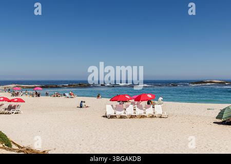 Ombrelloni rossi sulla spiaggia soleggiata di Camps Bay, un sobborgo di città del Capo sulla costa occidentale della Penisola del Capo Foto Stock