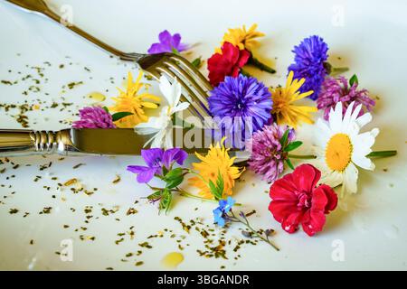 Teste di fiori colorati con spezie e gocce di olio d'oliva su Un piatto di porcellana con posate. I fiori sono spesso usati come decorazioni commestibili per Dishe Foto Stock