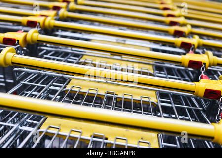 Primo piano dei carrelli gialli. Carrelli in metallo impilati in fila. Apparecchiature per supermercati pronte per l'uso. Simbolo del consumismo e dell'economia al dettaglio. Foto Stock