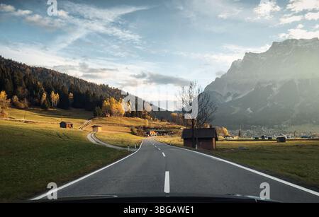 Strada vuota nella valle di montagna sotto i raggi del sole del mattino. Guida su strade curve nella campagna alpina del Tirolo, il monte Zugspitze e il Wetterstein Foto Stock