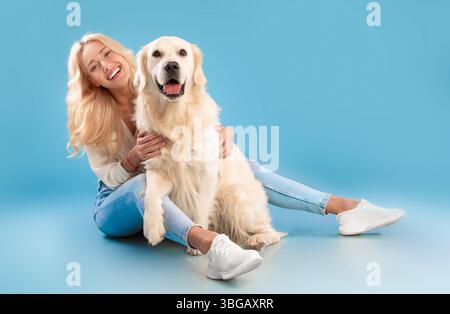 Giovane donna seduta con il suo cane allo studio blu Foto Stock