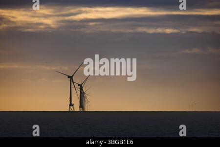 Le turbine eoliche offshore si stagliano contro un cielo arancione al tramonto nel Mare del Nord. Infrastrutture per le energie rinnovabili in acque calme. Foto Stock