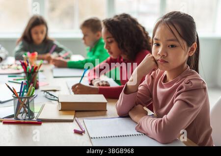 Infelice Asian Schoolgirl pensare seduta con diversi compagni di classe in classe Foto Stock