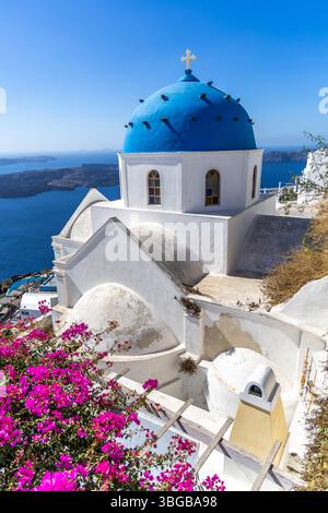 Santorini, Grecia - 15 ottobre 2024: Santorini, Grecia - 15 ottobre 2024: Classica chiesa a cupola blu a Santorini con fiori colorati e panoramica Foto Stock