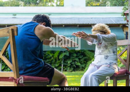 Fisioterapista che assiste una donna anziana con esercizi di riabilitazione in un vivace giardino domestico, migliorando la salute e la mobilità e promuovendo al contempo una guarigione Foto Stock
