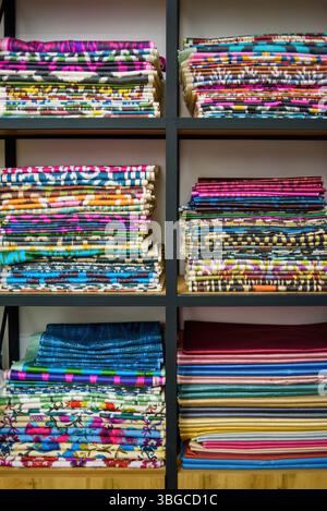 Colorate pile di tradizionali tessuti ikat uzbeki sugli scaffali di un negozio di tessuti, che mostrano vivaci motivi e ricco patrimonio culturale dell'Uzbekistan Foto Stock