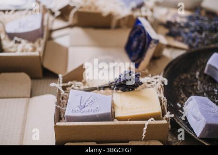 Saponi di lavanda e gialli fatti a mano con loghi stampigliati posizionati in scatole kraft con fiori secchi. Sapone fatto a mano, marchio artigianale, logo stampato Foto Stock