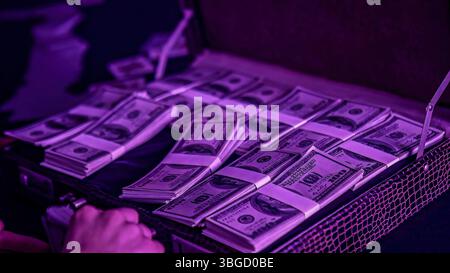 Valigia aperta piena di pile di banconote da cento dollari sotto la luce viola Foto Stock