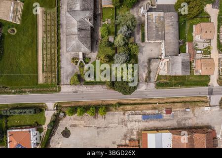 La prospettiva aerea cattura una tranquilla strada di campagna che separa edifici residenziali e campi coltivati, mostrando una miscela di rurale e urbano Foto Stock