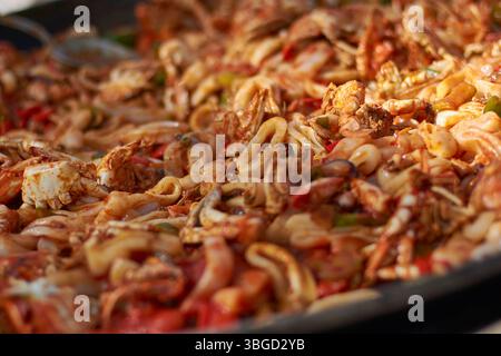 Primo piano di una deliziosa paella di pesce, con gamberi, calamari, granchi e verdure in una salsa ricca e saporita Foto Stock