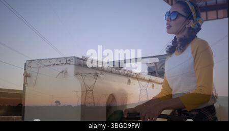 Immagine di pali elettrici sopra donna caucasica che fa rifornimento di auto Foto Stock