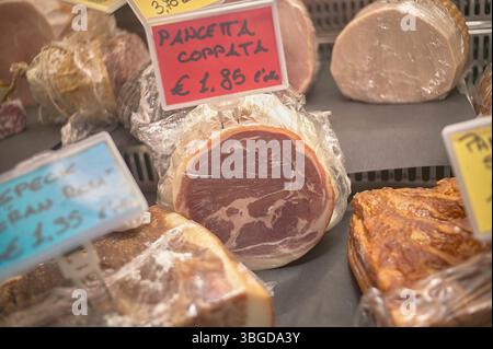 Milano, Italia 1° gennaio 2025: Deliziosa pancetta, speck e altri salumi avvolti in pellicola di plastica, esposti in vendita in una macelleria Foto Stock