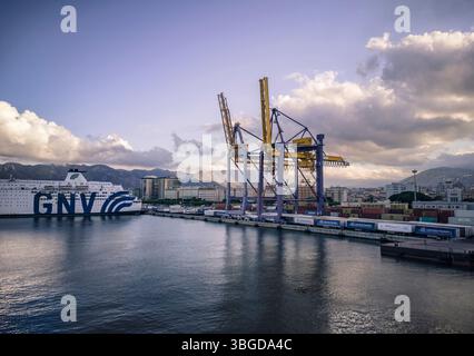 Palermo, Italia 1° gennaio 2025: Un traghetto gnv è attraccato nel porto di palermo, con gru e container che si riflettono nell'acqua calma sotto una nuvolosa Foto Stock