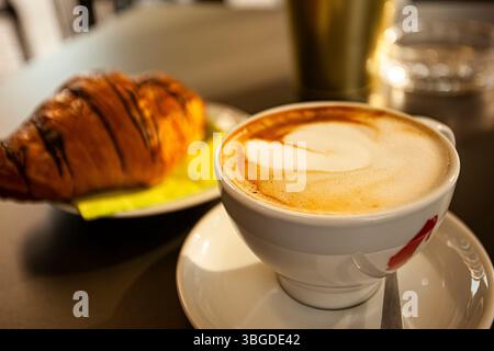 Verona, Italia 1 gennaio 2025: Cappuccino cremoso decorato con schiuma a forma di cuore servito con un croissant fresco per una deliziosa colazione a verona, i Foto Stock