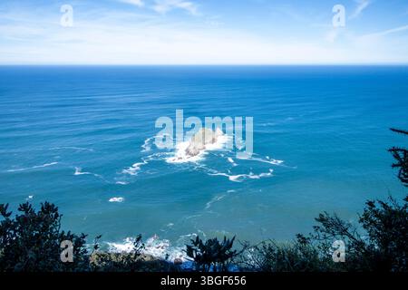 Vista mozzafiato di un piccolo isolotto roccioso circondato dalla vastità dell'oceano blu profondo, con un cielo sereno e nuvoloso in alto Foto Stock