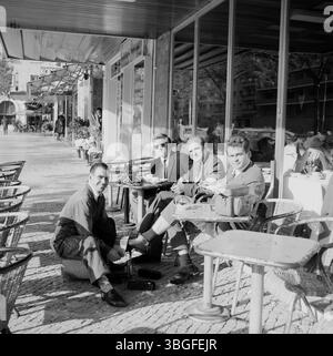 Drei Männer sitzen in einem Straßencafé in Lissabon und genießen Kaffee, während ein Schuhputzer Klaus Redenbacher Die Schuhe poliert. Die Szene entstand 1963 und vermittelt ein typisches Bild portugiesischer Alltagskultur im öffentlichen Raum. Foto Stock