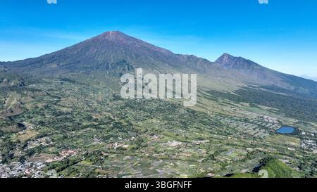 Maestosa veduta aerea del Monte Rinjani che sorge sopra la lussureggiante valle di Sembalun. Le pendici vulcaniche e i terreni agricoli creano un paesaggio mozzafiato a Lomb Foto Stock