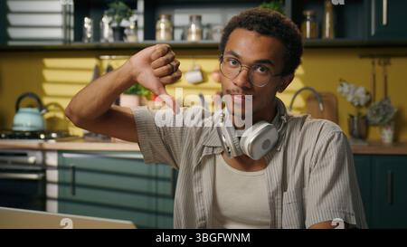 Ragazzo serio uomo afroamericano maschio studente gen z freelancer uomo d'affari istruzione a distanza laptop lavoro in cucina a casa mostrando un gesto verso il basso con il pollice Foto Stock