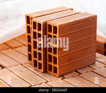 Diversi mattoni cavi in terracotta sono impilati ordinatamente su un pallet di legno in un cantiere, pronti per essere utilizzati nella costruzione di una nuova struttura Foto Stock