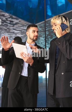 Uomini d'affari che lavorano insieme con tablet e telefono in un moderno ufficio in vetro Foto Stock