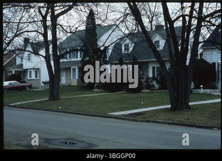 Una scena di strada non identificata caratterizzata da case a due piani con telaio in legno distanti dalla strada. Una casa ha una facciata parziale in pietra e l'altra presenta un tetto di gamberi con due finestre dormitori. Foto Stock