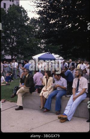 Questa immagine del 1980 mostra le persone riunite sul terreno dell'Ohio Statehouse. I partecipanti si concentrano su qualcosa al di fuori dell'inquadratura, con un uomo che tiene una videocamera vicino a un ombrello bianco e blu. Foto Stock