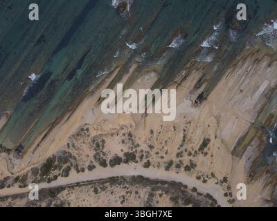 Vista dall'alto verso il basso con drone della costa frastagliata di Cap de l'Horta ad Alicante, che mostra impressionanti formazioni rocciose e strutture costiere mediterranee. Foto Stock