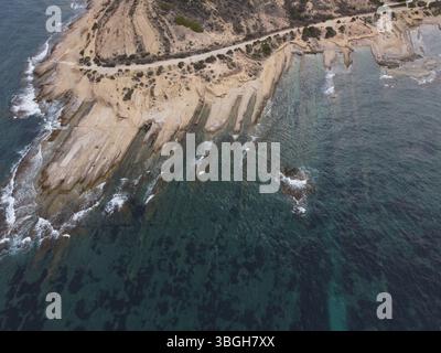 Vista dall'alto verso il basso con drone della costa frastagliata di Cap de l'Horta ad Alicante, che mostra impressionanti formazioni rocciose e strutture costiere mediterranee. Foto Stock