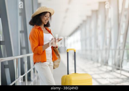 Ritratto della bella donna nera che usa lo smartphone mentre aspetta all'aeroporto Foto Stock