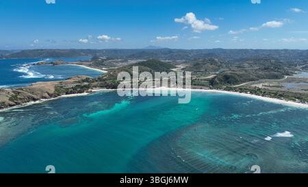 Le acque turchesi e le spiagge di sabbia bianca si snodano lungo la costa di Lombok. Colline ondulate e strade tortuose si estendono nell'entroterra sotto un luminoso cielo tropicale. Foto Stock