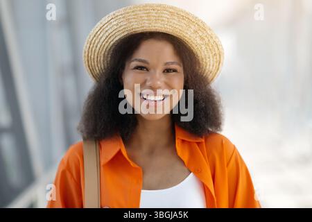 Allegra viaggiatrice millenaria nera che indossa un cappello di paglia in posa al terminal dell'aeroporto Foto Stock