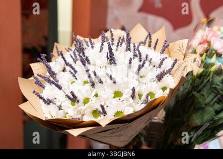 Bouquet rustico di margherite bianche fresche e ciuffi di lavanda, splendidamente avvolti in carta kraft, perfetto per regali o decorazioni. Foto Stock